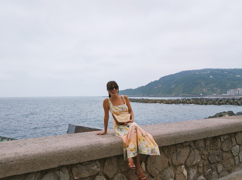 Woman in a dress sitting on the sea wall around San Sebastian, Spain